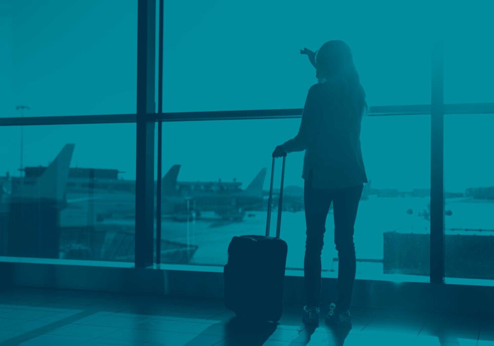 Young traveller with suitcase at airport window, representing student travel insurance cover for dependants in Europe